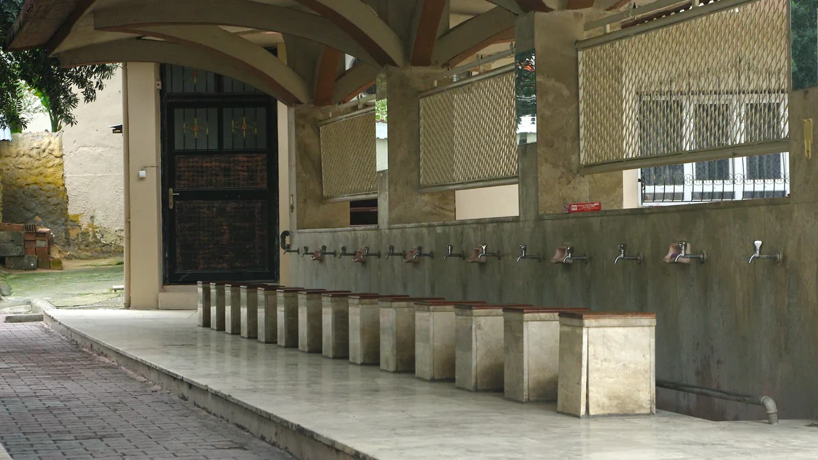 La fontaine aux ablutions de la Grande Mosquée de Kozan, en Turquie : une rangée de robinets au-dessus de sièges de pierre, sous un auvent