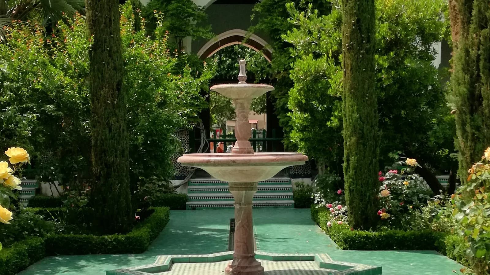 Une fontaine de marbre au milieu du jardin de la Grande Mosquée de Paris, entre cyprès et rosiers