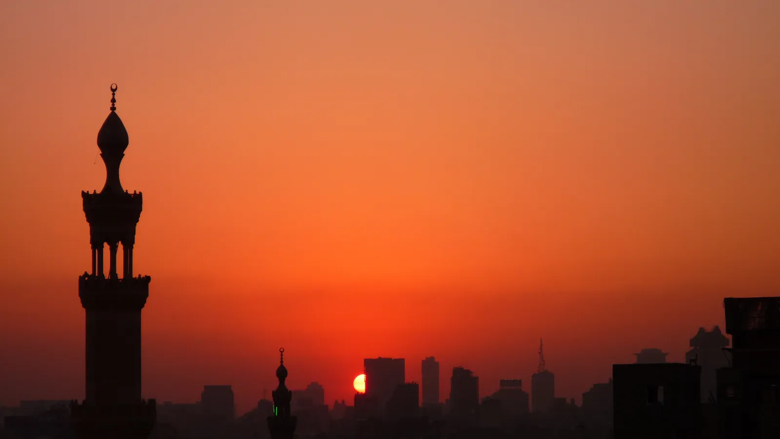 Silhouette d’un minaret du Caire sur un ciel orange, au moment où le soleil se couche derrière la ville