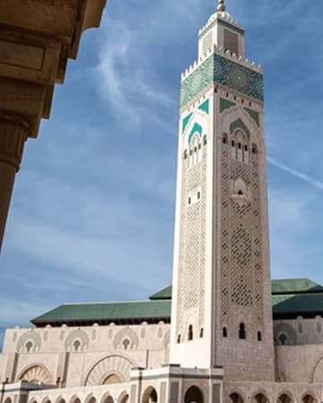 Un haut minaret carré orné de zellige vert, sous un ciel bleu